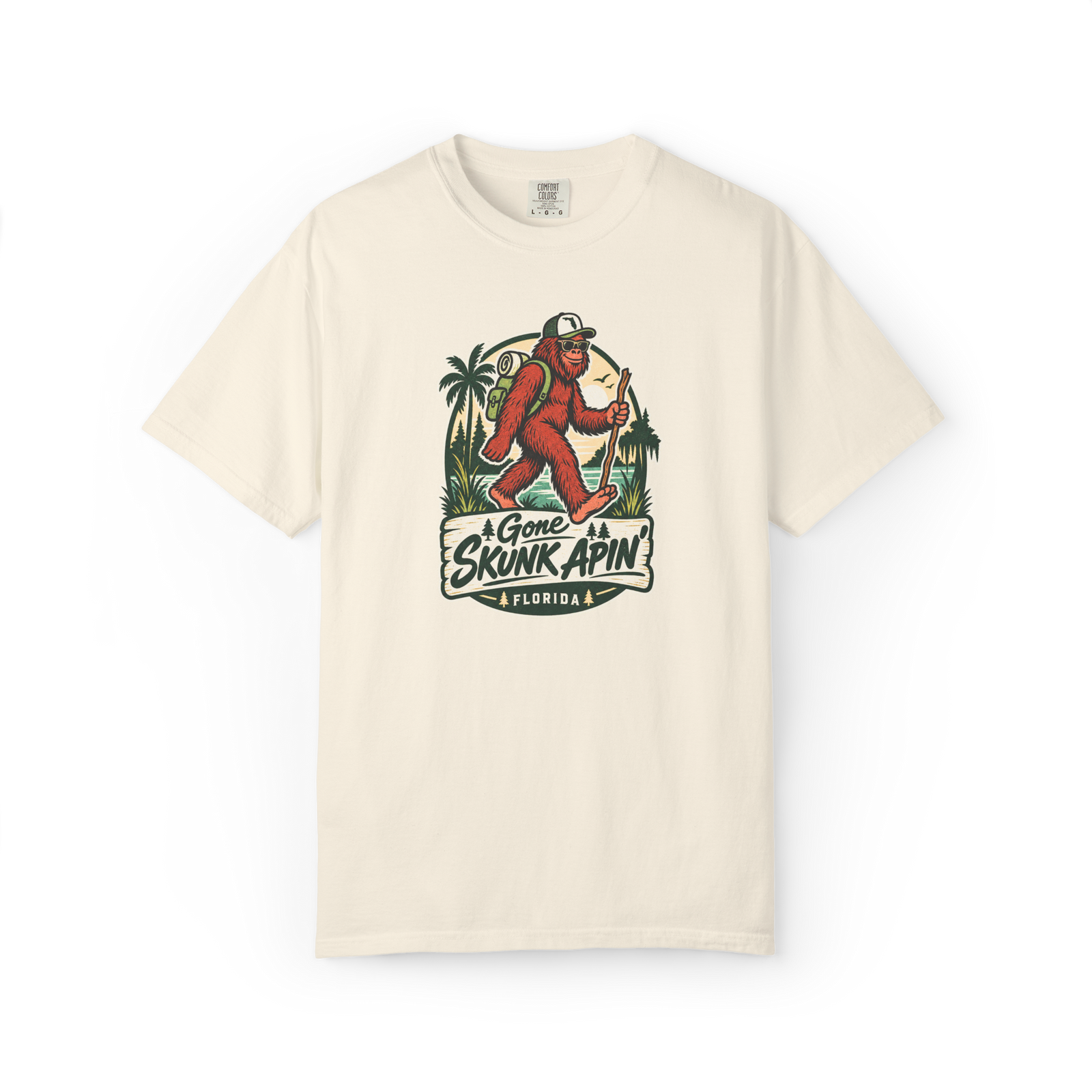Ivory Gone Skunk Apin t shirt with a red-brown hiking Skunk Ape wearing sunglasses and carrying a backpack in a Florida outdoor scene