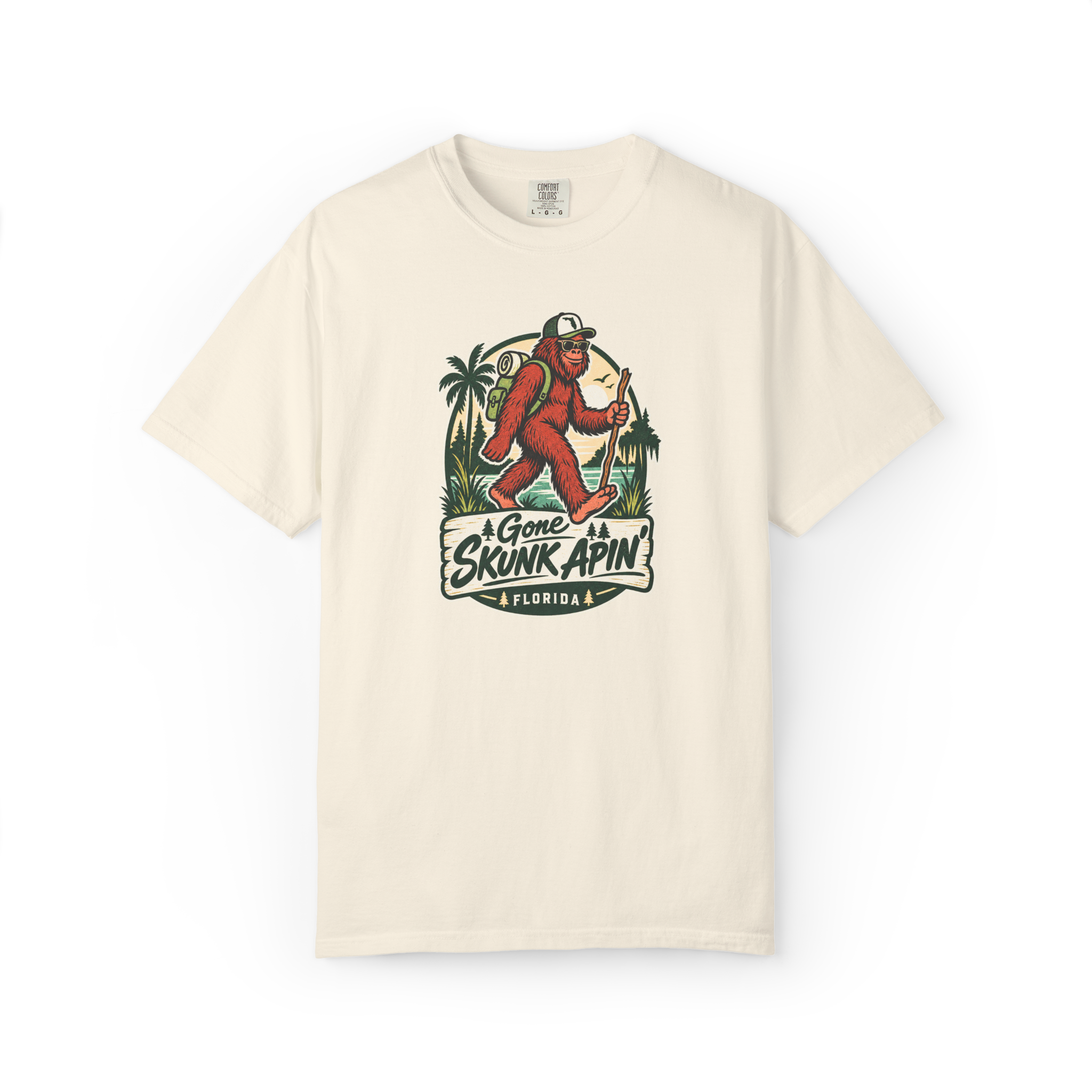 Ivory Gone Skunk Apin t shirt with a red-brown hiking Skunk Ape wearing sunglasses and carrying a backpack in a Florida outdoor scene