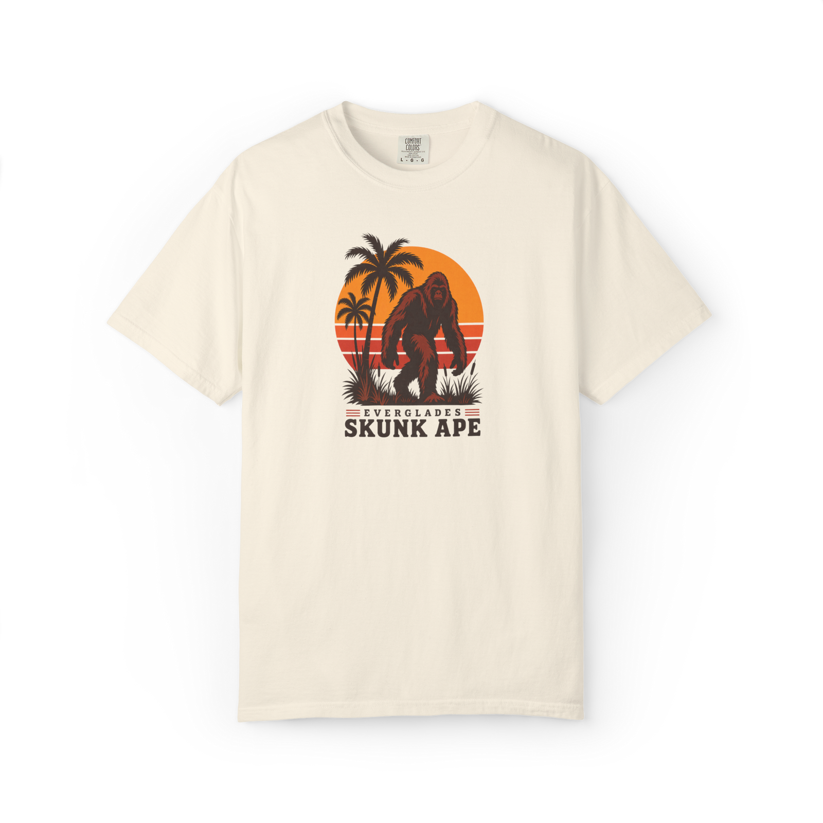Ivory Everglades Skunk Ape t shirt with a full-body red-brown skunk ape, palm trees, sunset stripes, and Everglades Skunk Ape text