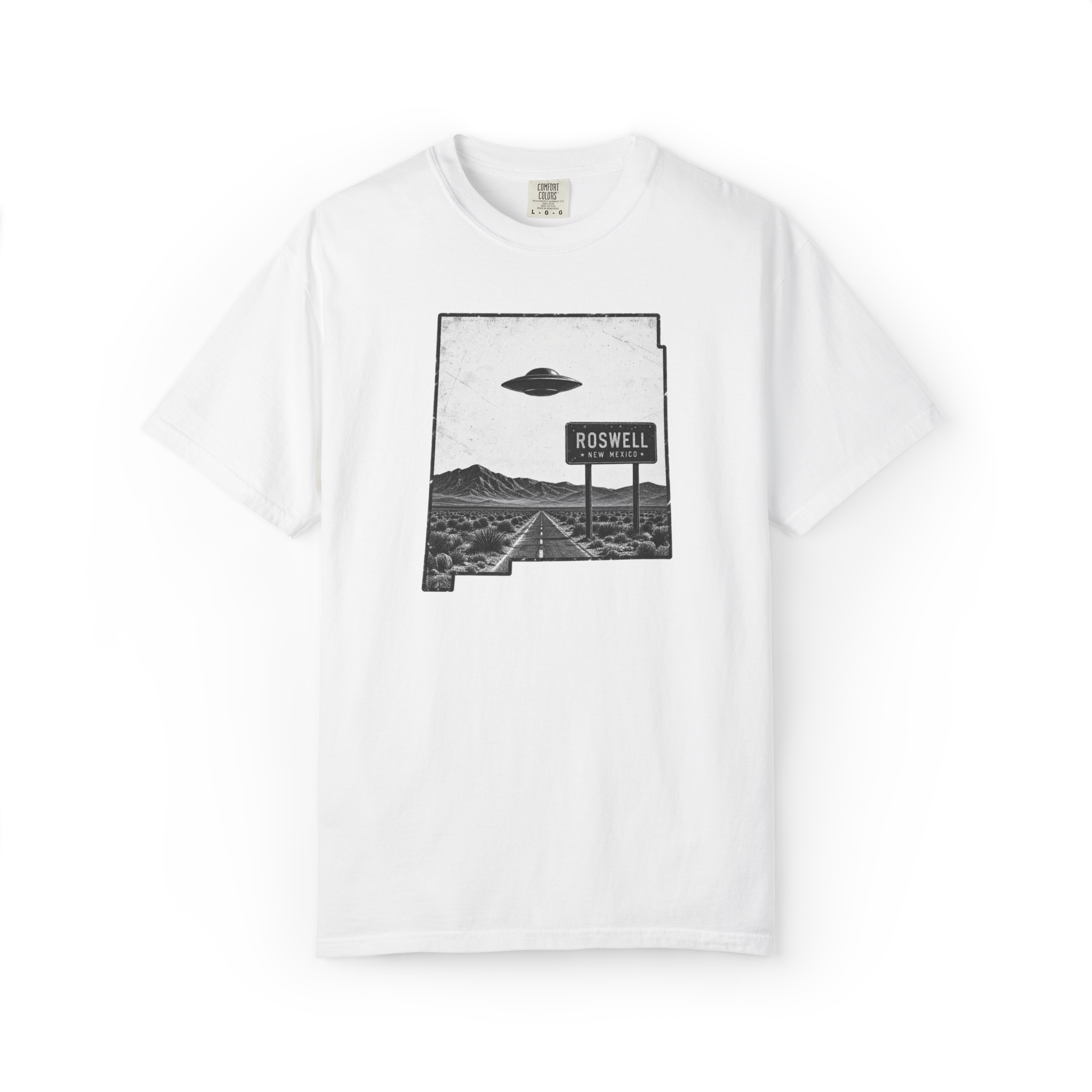 White Roswell UFO shirt featuring a flying saucer over a desert highway with Roswell New Mexico road sign inside the New Mexico state outline